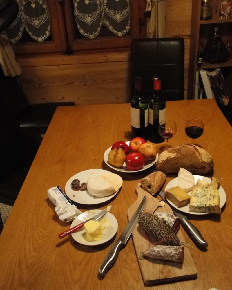 Plusieurs assiettes avec du fromage, de la charcuterie, du vin sur une table en bois rustique